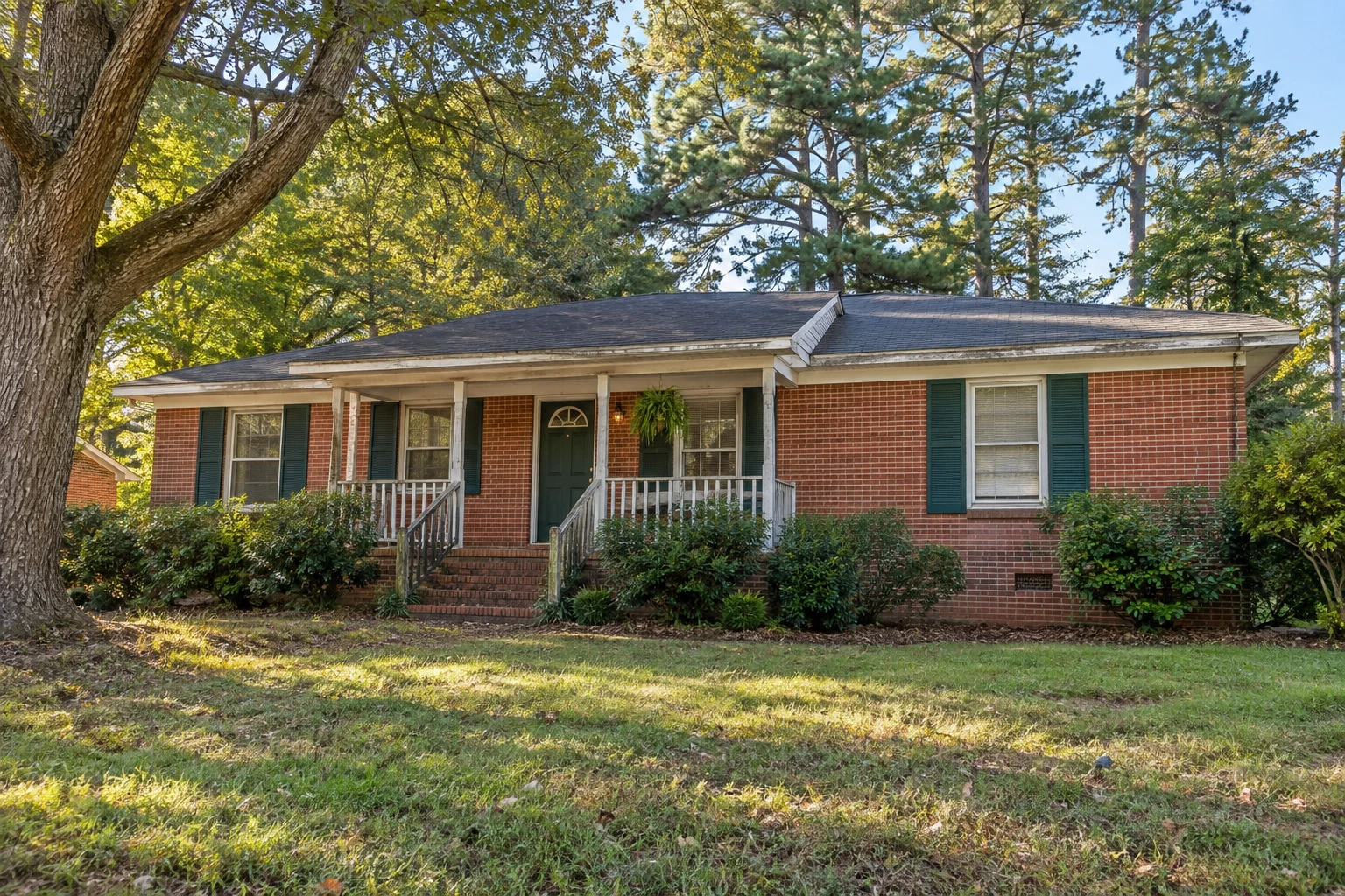 Older brick ranch with weathered trim and green shutters.