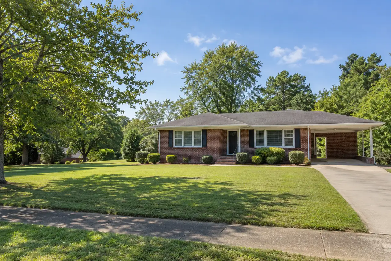 Illustrative scene: a 1960s low red-brick ranch house with a carport and a wide lawn in High Point, North Carolina